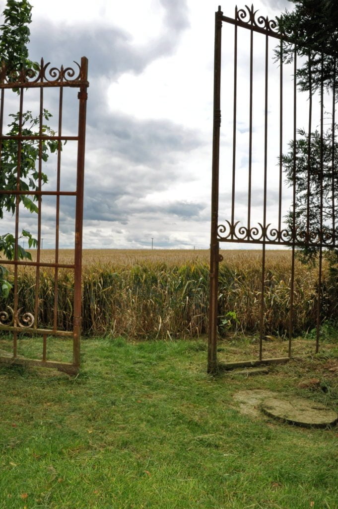 Ancien portail métallique ouvert sur un champ sous un ciel nuageux